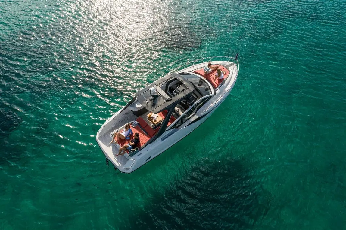 Aerial view of a sleek motorboat on clear turquoise water, with four people enjoying leisure time on board.